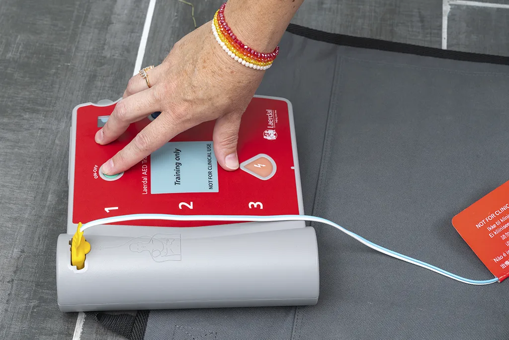 Main appuyant sur le bouton d’un DAE lors d’une démonstration en formation défibrillateur