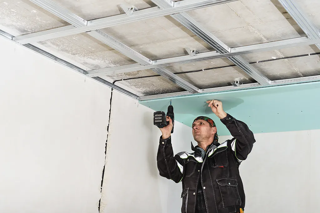 Employé utilisant une perceuse sous un plafond, intervenant dans un environnement électrique avec précautions