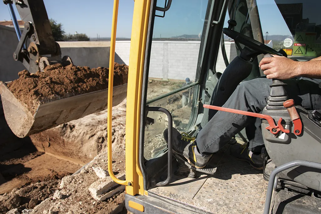 Excavatrice en action sur un chantier de construction, opérée par un conducteur d’engins